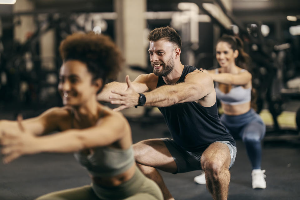 Fit friends in a squat position exercising with an instructor in a gym.