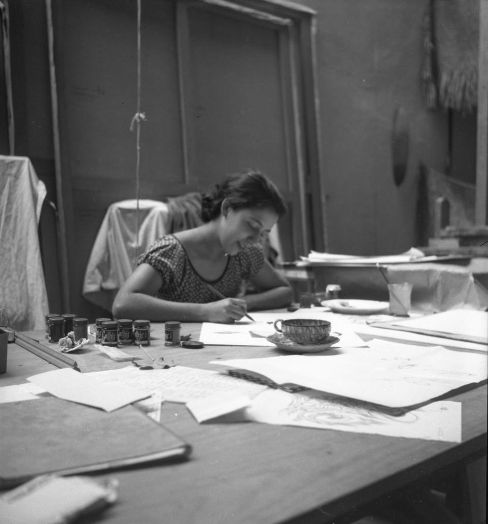 A 1945 black-and-white snapshot shows Luchita Hurtado painting at a large table.