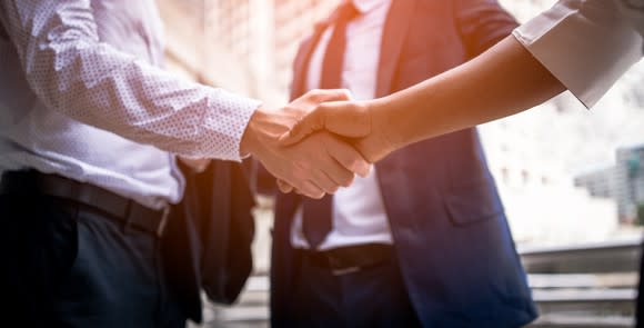 Two businessmen shaking hands in front of another businessman in a suit