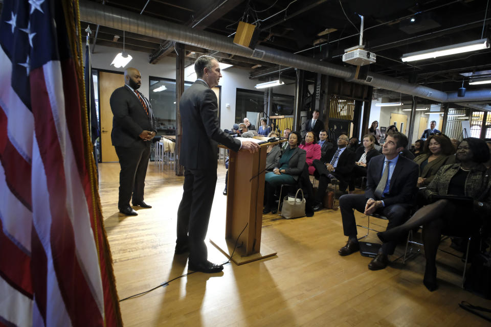 As Del. Lamont Bagby, D-Henrico, left, looks on, Gov. Ralph Northam, at podium, addresses a gathering after receiving the report from The Commission to Examine Racial Inequity in Richmond, Va., Thursday, Dec. 5, 2019. (Bob Brown/Richmond Times-Dispatch via AP)