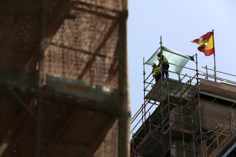 FILE PHOTO: Workers stand next to a Spanish flag at a construction site in Madrid