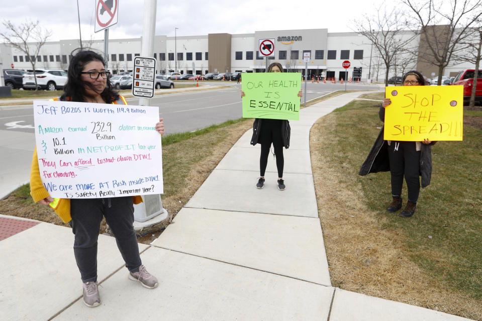 FILE - In this April 1, 2020, file photo, Breana Avelar, left, a processing assistant and family members, hold signs outside the Amazon DTW1 fulfillment center in Romulus, Mich. Even after Amazon scrambled to provide masks and gloves and check employees’ temperatures, workers continue conducting scattered walkouts across the country to protest what they say are still-risky conditions in warehouses where workers have had the virus. (AP Photo/Paul Sancya, File)
