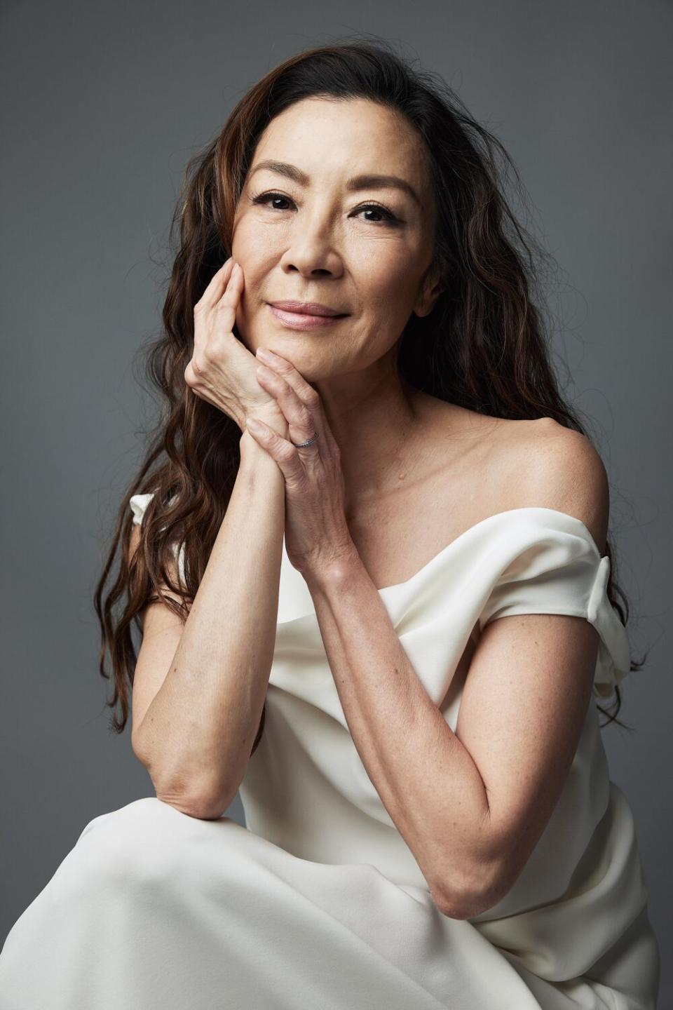 A seated woman in a white off-the-shoulder dress cups her face in one hand.