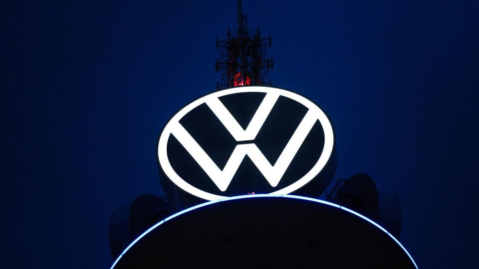 Das Volkswagen Logo leuchtet auf dem VW-Tower vor dunklem Himmel.