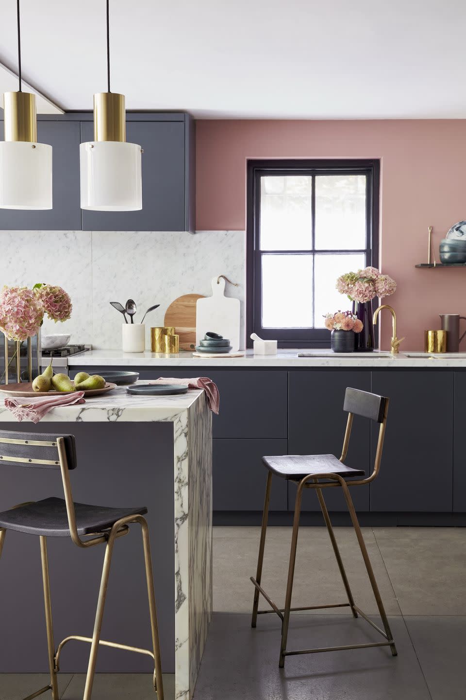 a grey kitchen with dark grey units, pink walls and a marble breakfast bar with two bar stools