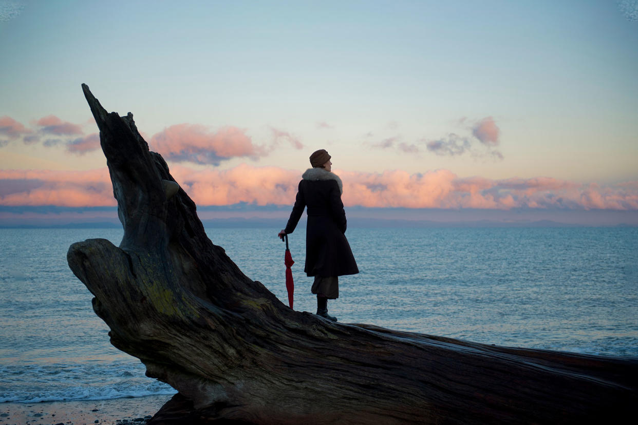 Woman leaning on umbrella standing on large driftwood tree trunk on beach Getty Images/Pete Saloutos
