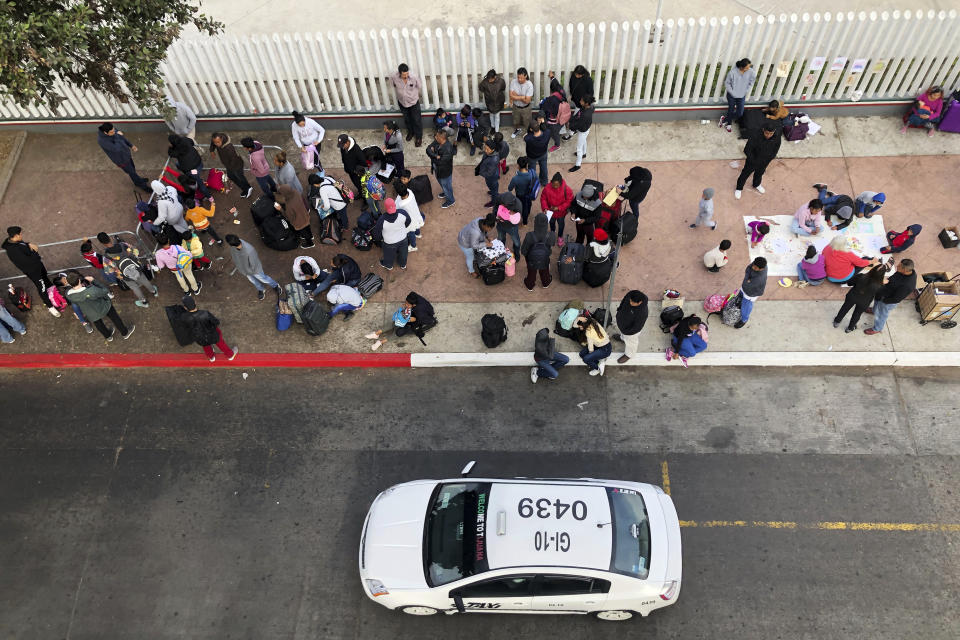 FILE - In this Nov. 10, 2019, file photo, migrants gather at the U.S.-Mexico border in Tijuana, Mexico, to hear names called from a waiting list to claim asylum in the U.S. U.S. authorities wield extraordinary power available in public health emergencies, like the coronavirus pandemic, to expel Mexicans and many Central Americans immediately to Mexico and waive immigration laws that include rights to seek asylum. (AP Photo/Elliot Spagat, File)