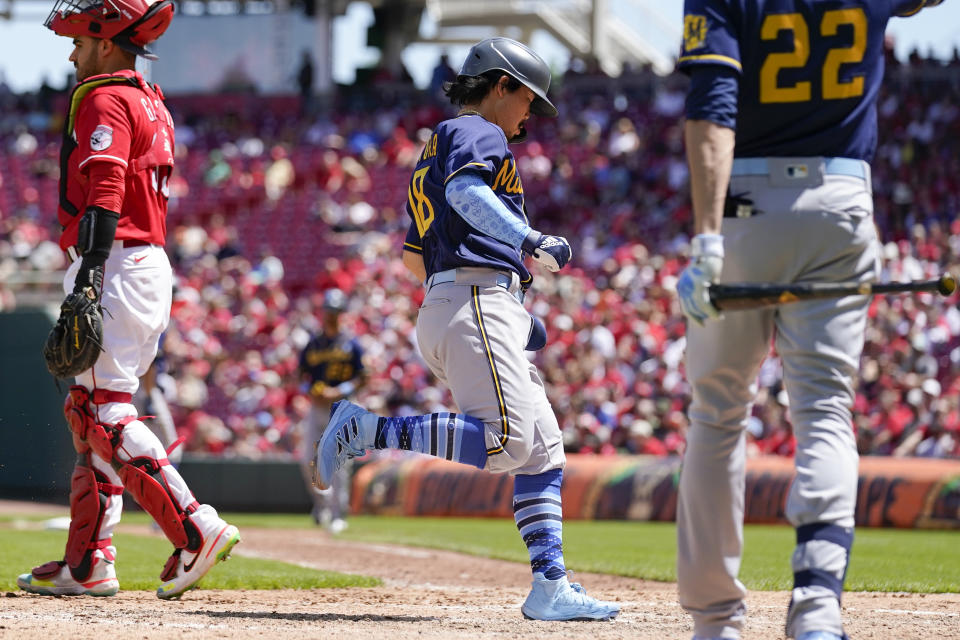 Milwaukee Brewers' Keston Hiura, center, scores on a sacrifice fly ball hit by Mark Mathias during the sixth inning of a baseball game against the Cincinnati Reds, Sunday, June 19, 2022, in Cincinnati. (AP Photo/Jeff Dean)