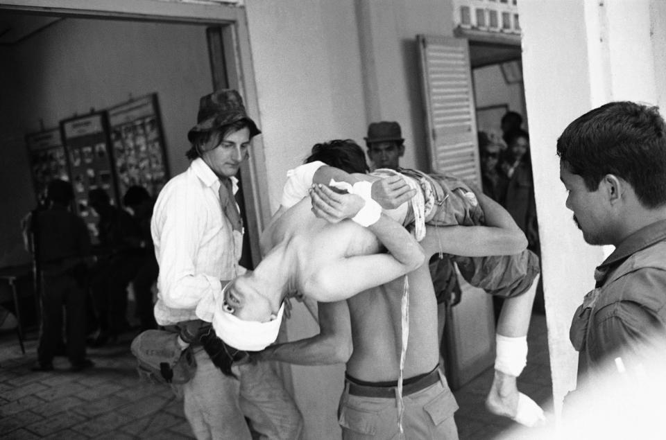 FILE - In this May 18, 1970, file photo taken by Max Nash, a bandaged North Vietnamese soldier is carried by a Cambodian soldier into the office of the Cambodian military region 1 commander at Kompong Cham in Cambodia. Nash, who covered the conflicts in Southeast Asia and the Middle East and helped nurture a new generation of female photojournalists during more than 40 years with The Associated Press, died Friday, Sept. 28, 2018, after collapsing at home. He was 77. (AP Photo/Max Nash, File)