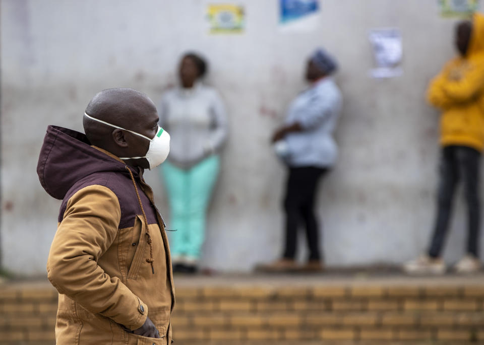 Un hombre que porta un cubrebocas como medida ante el coronavirus camina enfrente de personas formadas para realizar compras en Duduza, al este de Johannesburgo, Sudáfrica, el jueves 2 de abril de 2020. (AP Foto/Themba Hadebe)