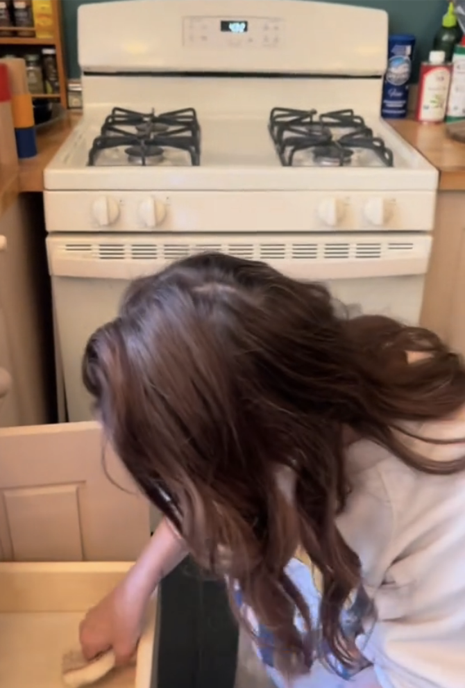 Drew  cleaning the kitchen counter beside a white stove