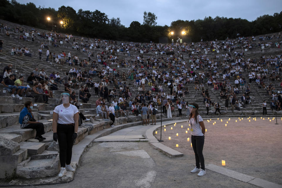 Stewards wearing surgical gloves and plastic visors stands as spectators take their seats at the ancient theater of Epidaurus, Greece, on Friday, July 17, 2020 Greek Culture Ministry allowed the ancient theaters of Epidaurus in southern Greece and Herodes Atticus in Athens to host performances under strict safety guidelines due the COVID-19 pandemic.(AP Photo/Petros Giannakouris)