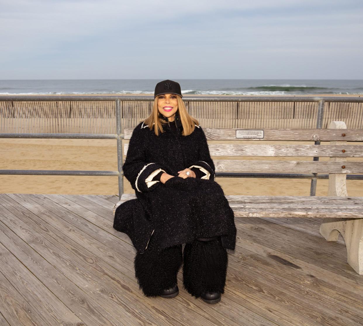 Wendy Williams seated on a boardwalk by the beach.