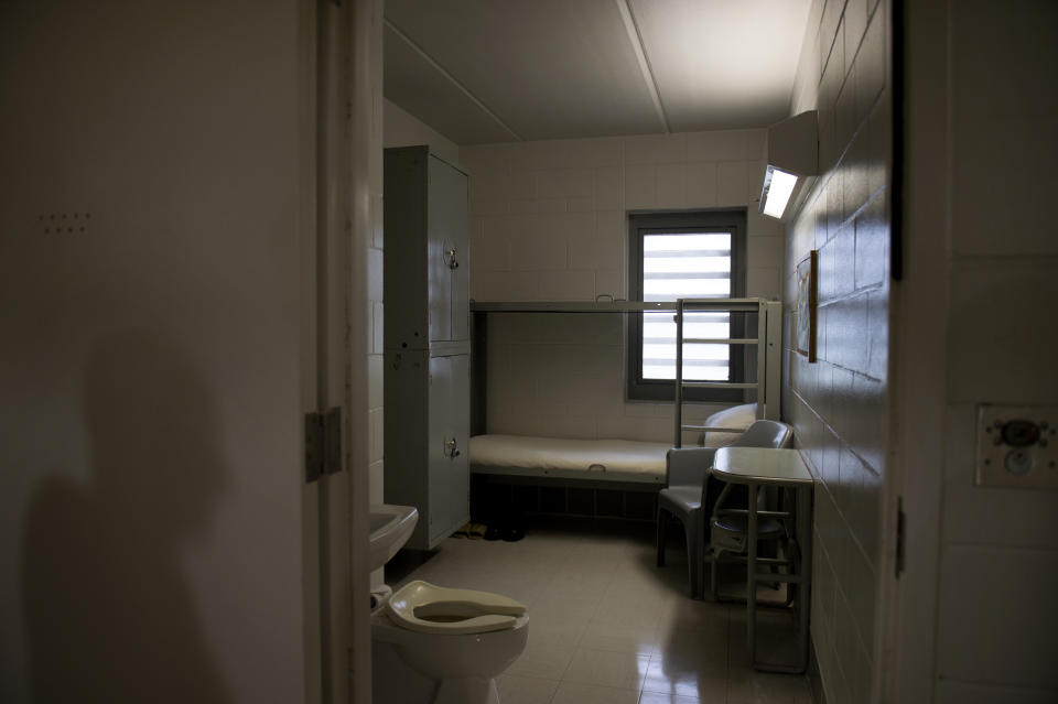 A federal prison cell with bunk bed, toilet, chair and lockers.