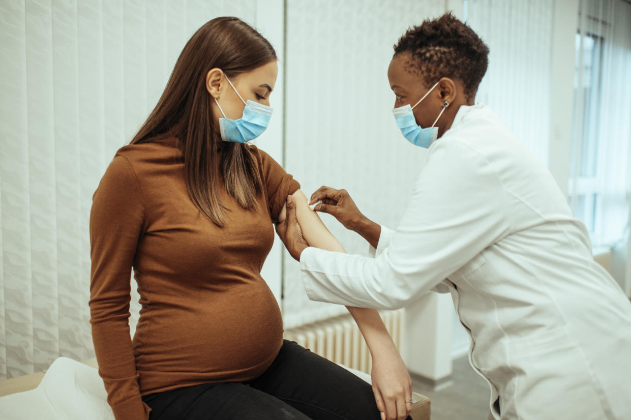 African American female doctor preparing a pregnant woman for vaccination. Pregnant woman getting a covid-19 vaccine.