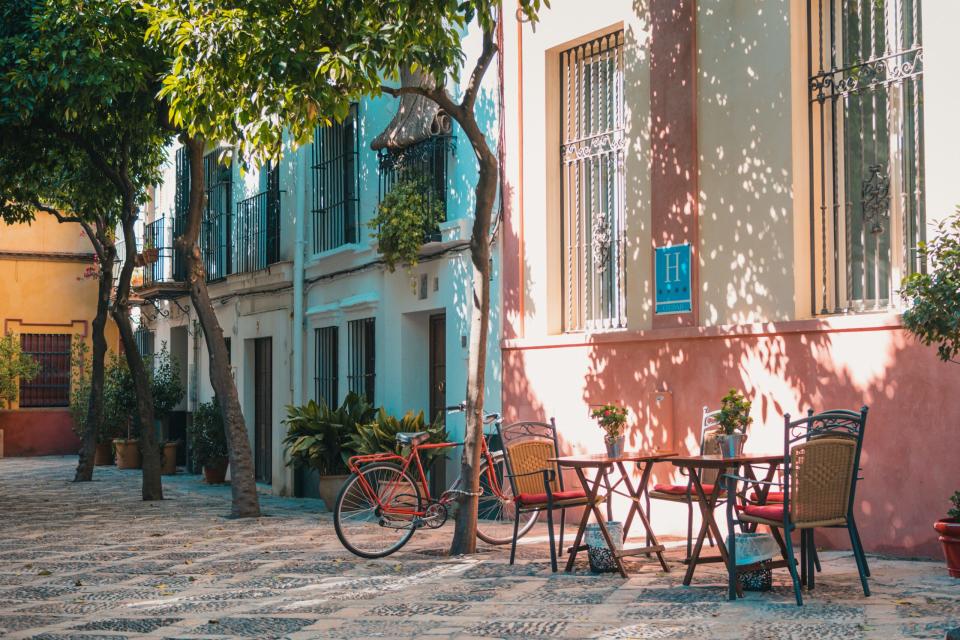 Check out the best cities to visit in Spain and what they offer travelers. 
Pictured: a city sidewalk of Spain with a cafe table surrounded by greenery