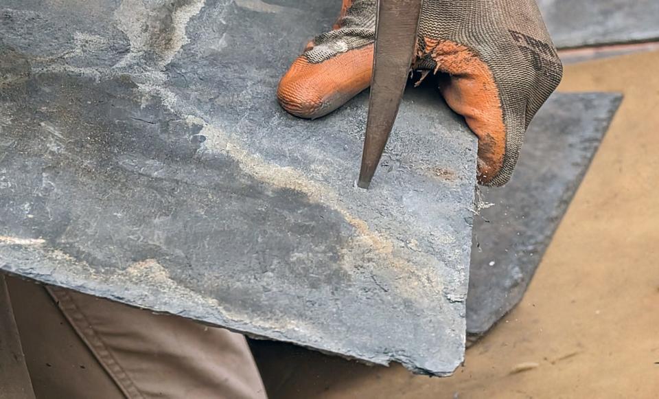 Ben Stewart uses a slater's hammer to instantly create a small hole that will be used to fasten the shingle to the roof with a copper nail.