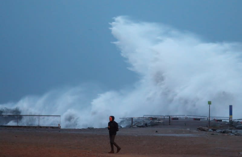 Man walks beside a sea wave during the storm "Gloria" on Barceloneta beach, in Barcelona