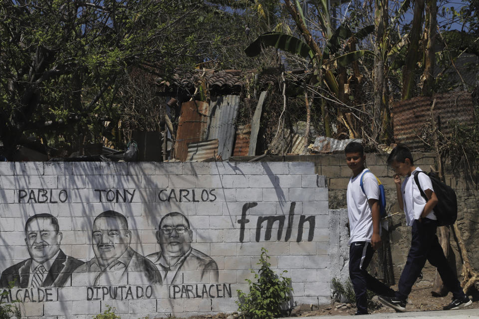 Students walk past a wall covered with the faces of candidates for mayor, national congress, and regional congress, all from the Farabundo Martí National Liberation Front (FMLN) party, in San Jose Las Flores, El Salvador, Wednesday, Feb. 28, 2024. El Salvador held its municipal elections on March 3, in which Pablo and Carlos won their contests, while Tony lost. (AP Photo/Salvador Melendez)