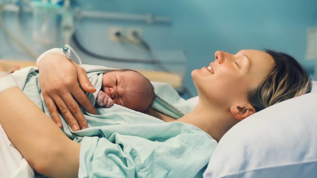 mother holding newborn baby in hospital bed and smiling possibly after using laughing gas for labor