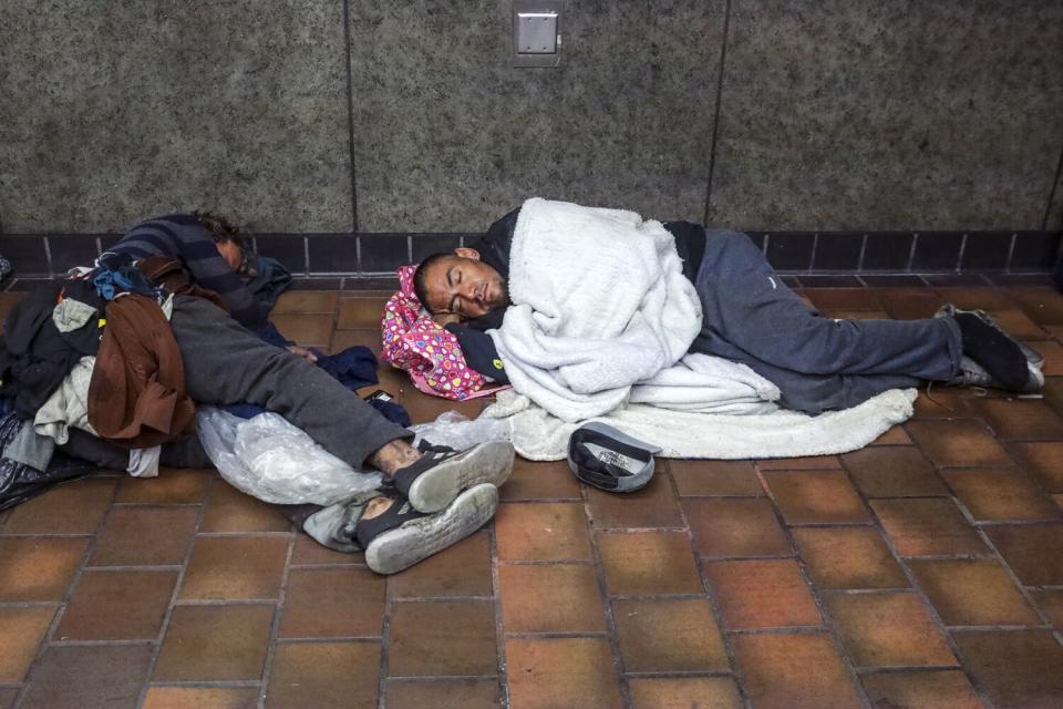 Homeless people sleep in front of the closed gates of 7th Street Metro station.