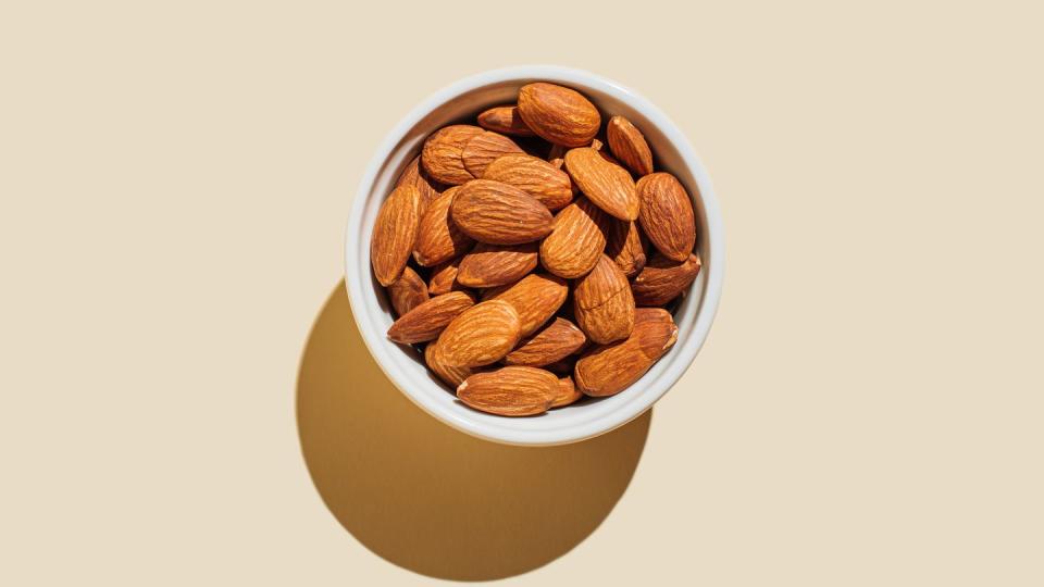 almond nuts in white bowl isolated on beige background minimal flat lay style top view, copy space