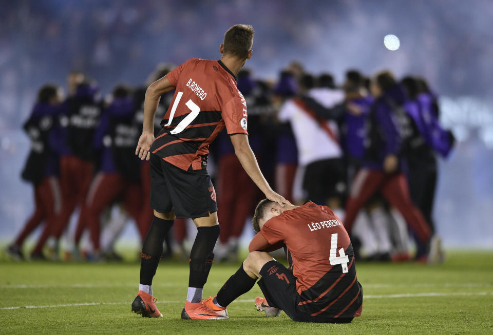 Leo Pereira of Brazil's Athletico Paranaense sits on the field as teammate Braian Romero pats him on the head after they lost the Recopa Sudamericana final soccer match 3-0 to Argentina's River Plate, celebrating behind, in Buenos Aires, Argentina, Thursday, May 30, 2019. (AP Photo/Gustavo Garello)