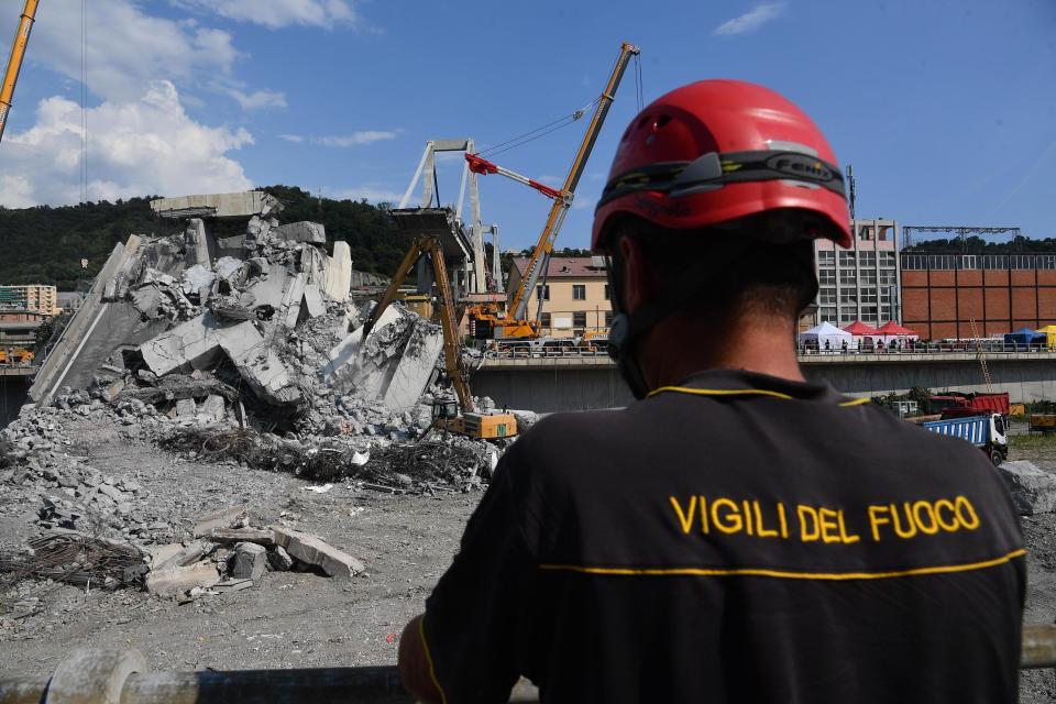 A firefighter looks at caterpillars as they clear debris from the collapsed Morandi highway bridge, in Genoa, Italy, Friday, Aug. 17, 2018. Officials say 38 people are confirmed killed and 15 injured. Prosecutors say 10 to 20 people might be unaccounted-for and the death toll is expected to rise. (Luca Zennaro/ANSA via AP)