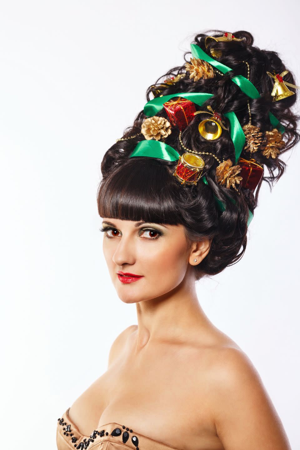 dark haired woman with thick bangs and tall beehive made into a christmas tree with green ribbon, gold pine cones, gold garland and ornaments throughout it