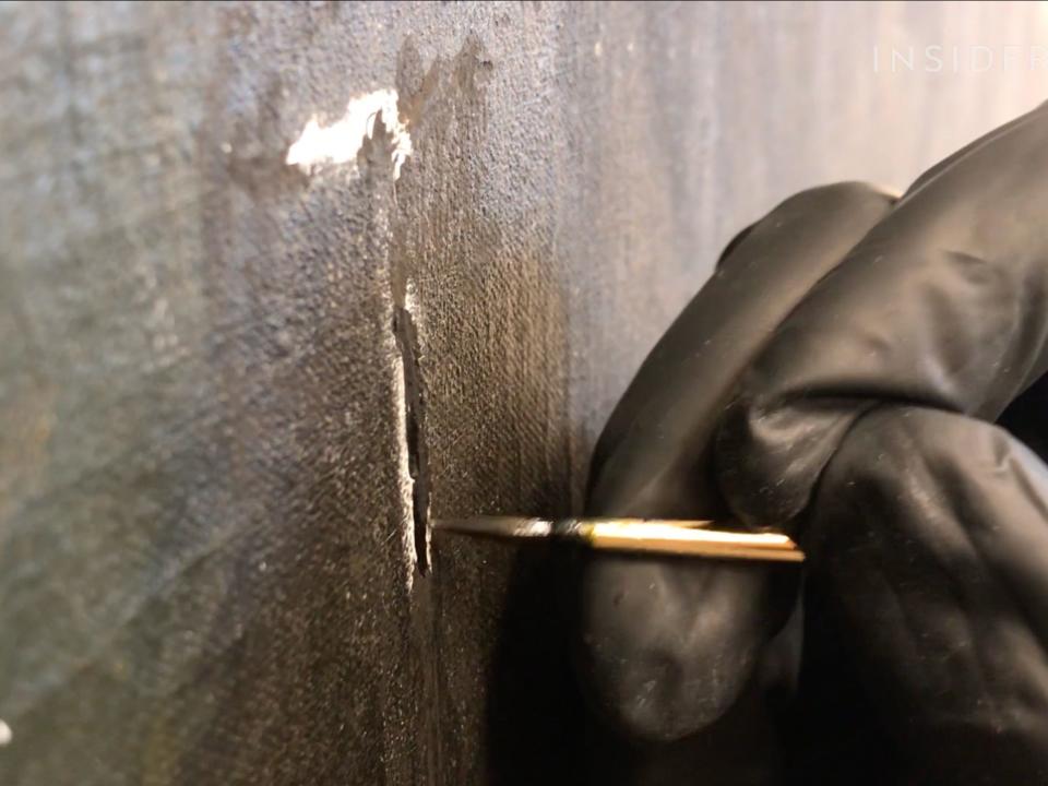 A conservator adds new paint to the painting.