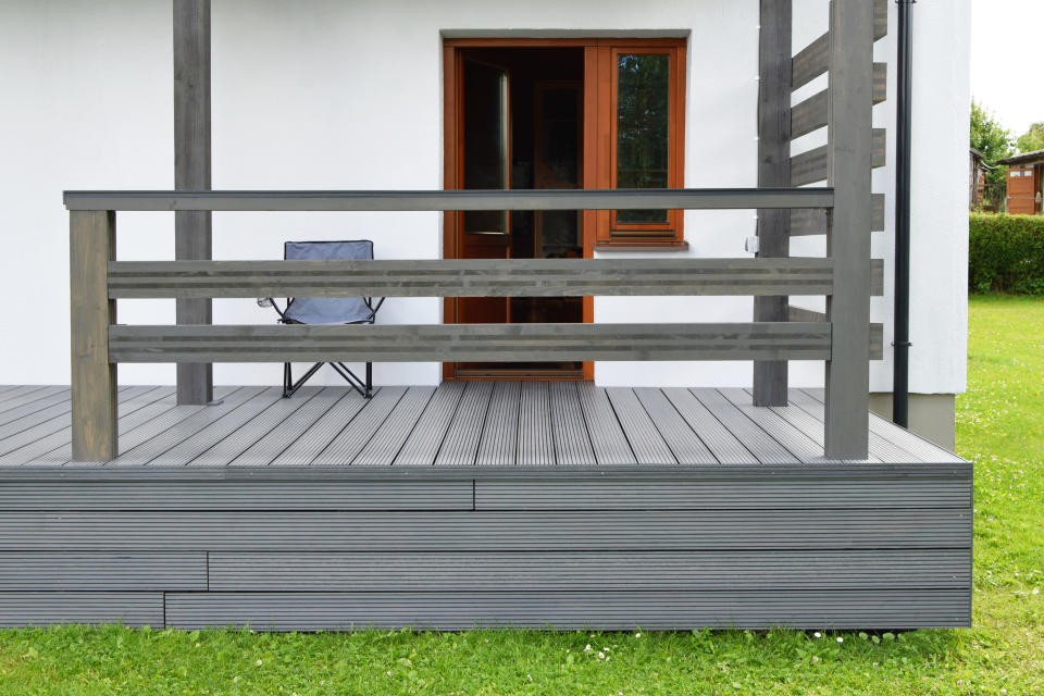 Wooden deck with modern railing in front of a house's open door, including an outdoor chair on the deck