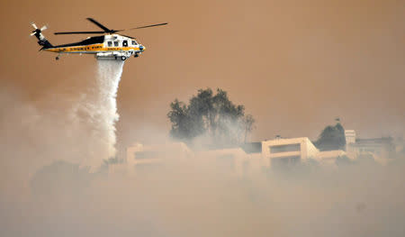 A Los Angeles County Fire Department firehawk makes a water drop through the thick smoke on homes in the hills of Malibu, as the Woosley Fire approaches, in California, U.S. November 9, 2018. REUTERS/Gene Blevins