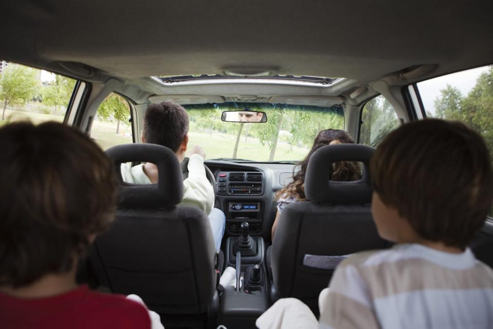 A camera in the back of a minivan captures two adults sitting in the front seat and two brunette children sitting in the back row.