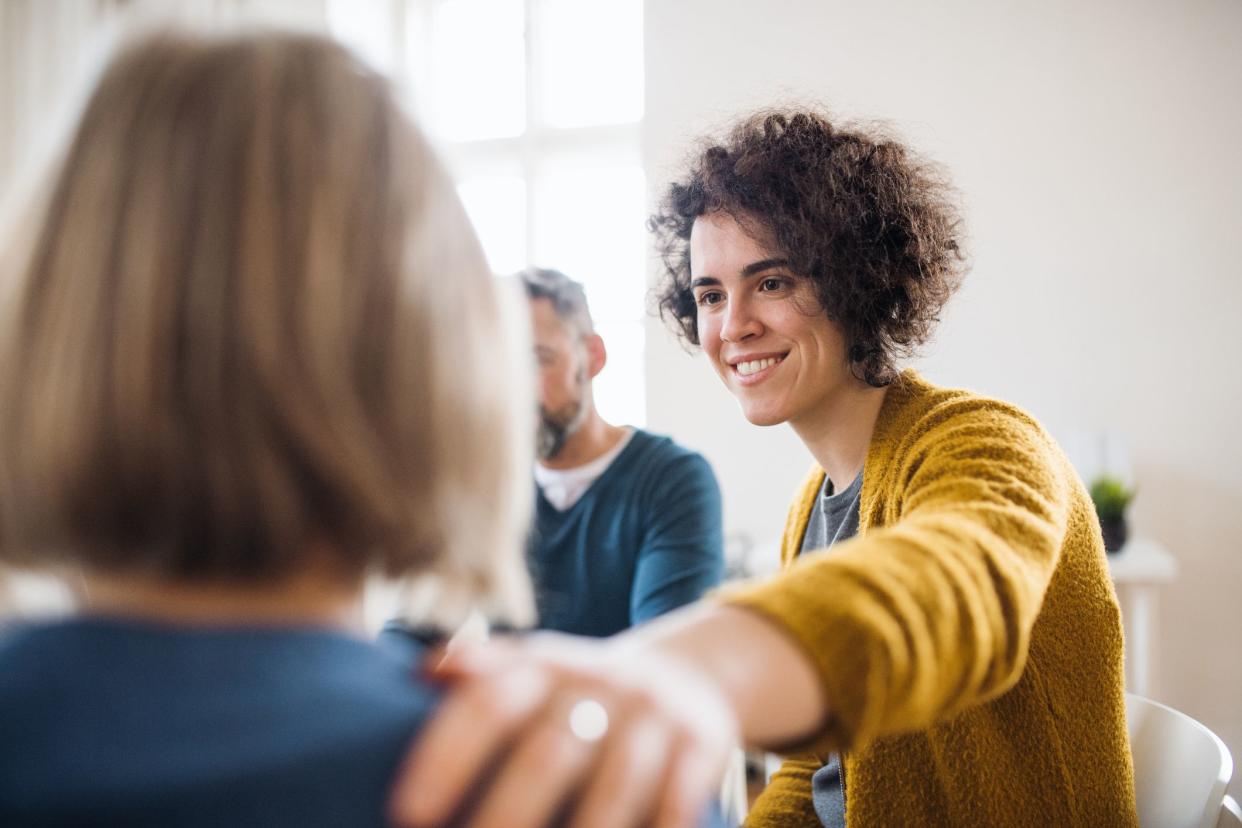 Serious men and women sitting in a circle during group therapy, supporting each other.