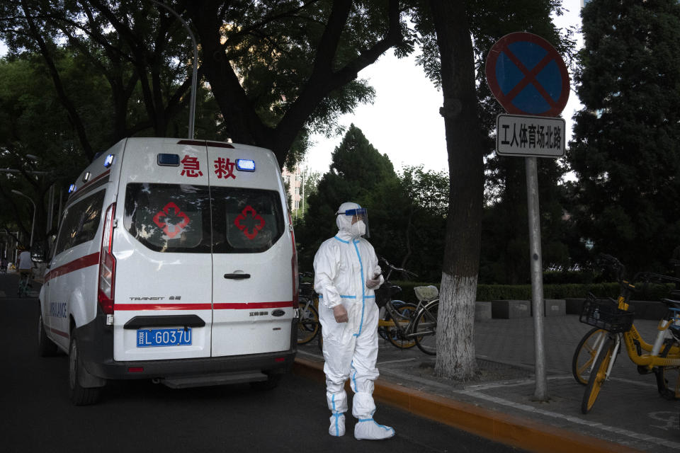 A worker wearing a protective suit to help protect against COVID-19 stands outside an ambulance parked along a street in Beijing, Thursday, May 26, 2022. (AP Photo/Mark Schiefelbein)