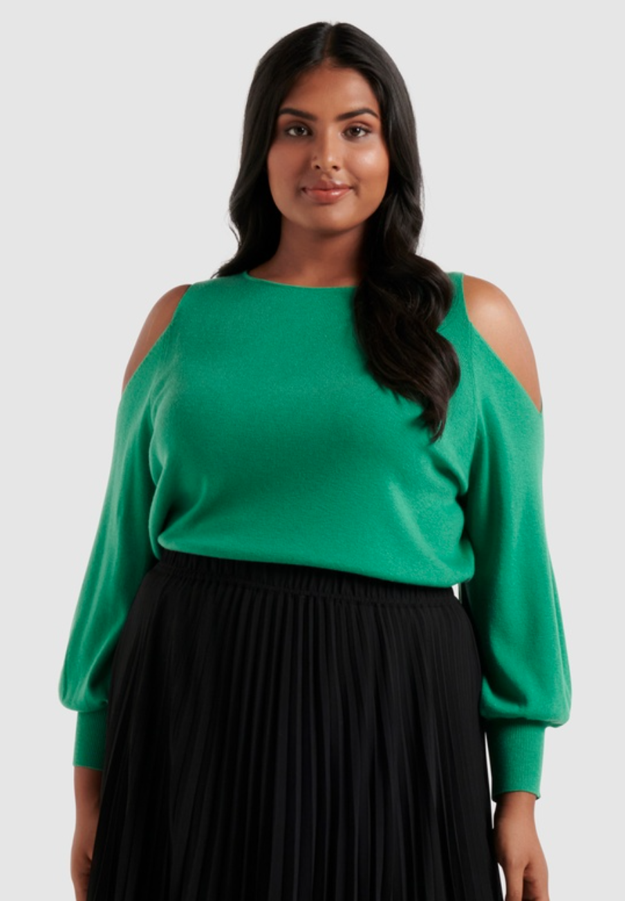 A model with long dark hair wears a bright green top with cutaway shoulders over black pants.