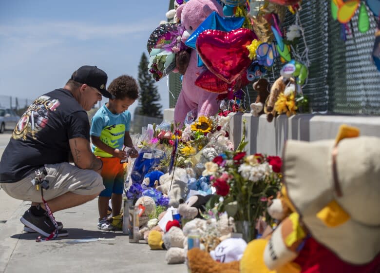 Orange, CA - May 25: Albert Lamonte helps his son, Marcel Lamonte, 2, of Huntington Beach, place flowers and a pinwheel at a growing makeshift memorial of balloons, toys, cards and candles to remember a 6-year-old boy who was shot and killed Friday during an apparent road rage incident on the 55 Freeway in Orange on Tuesday, May 25, 2021 in Orange, CA. "We drive this freeway all the time and e imagined if it was our little boy or girl," Lamonte said. (Allen J. Schaben / Los Angeles Times)