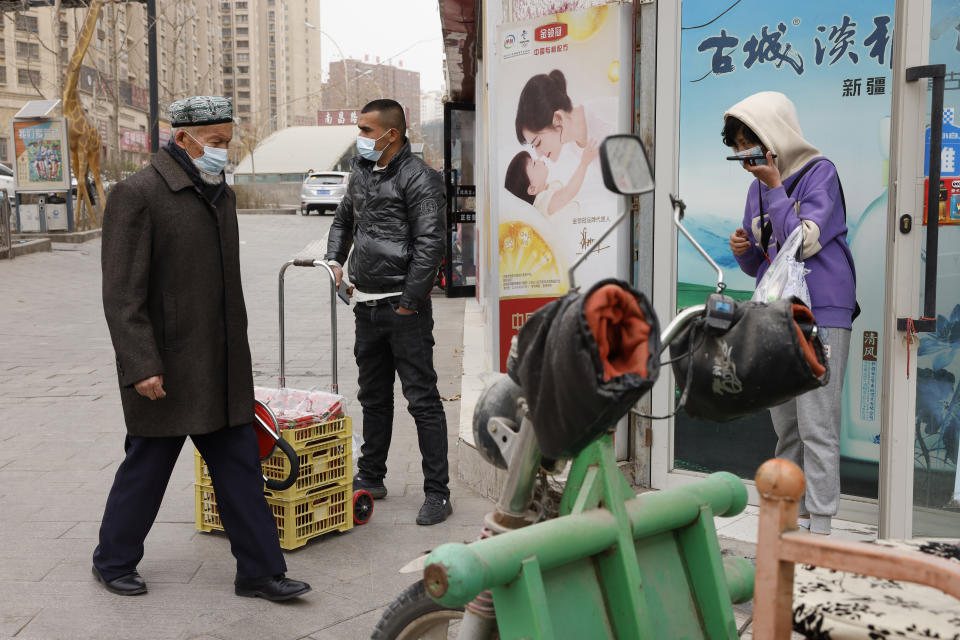 Residents wearing masks walk along the streets of Aksu in western China's Xinjiang region on Thursday, March 18, 2021. China on Friday announced sanctions on British individuals and entities following the U.K.'s joining the EU and others in sanctioning Chinese officials accused of human rights abuses in the Xinjiang region. (AP Photo/Ng Han Guan)