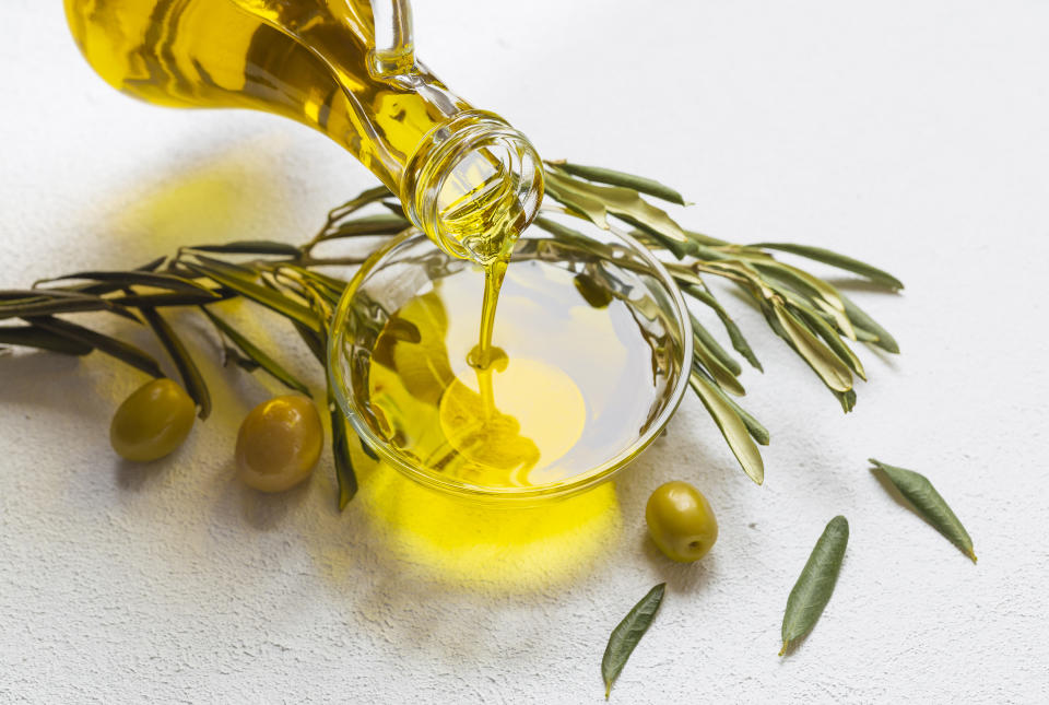 bottle pouring olive oil into a bowl surrounded by green olives and rosemary