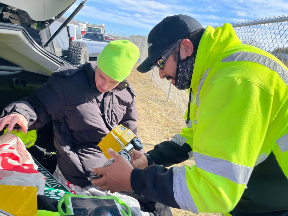 Rafael “Fito” Mata, a driver for WIN Waste Innovations, looks at one of Franklin Delano Stephen Everett's toy trucks. The commuter lot they are at, off of I-395 in Griswold, was unofficially named in Everett's honor on Friday. The official naming is still in the works.