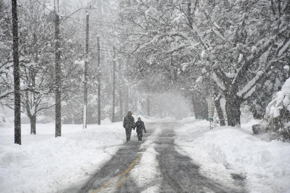 A couple of people walk on Dean Street in Cheshire, Mass., during a snowstorm on Tuesday, March 14, 2023. Much of the town, in Western Massachusetts, was without power due to downed lines. (Gillian Jones/The Berkshire Eagle via AP)