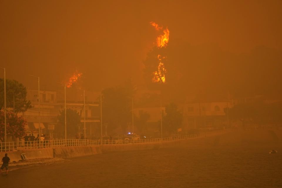 Fire burns trees near a beach at Pefki village on Evia island, about 189 kilometers (118 miles) north of Athens, Greece, Sunday, Aug. 8, 2021. Pillars of billowing smoke and ash are blocking out the sun above Greece's second-largest island as a days-old wildfire devours pristine forests and triggers more evacuation alerts. (AP Photo/Petros Karadjias)