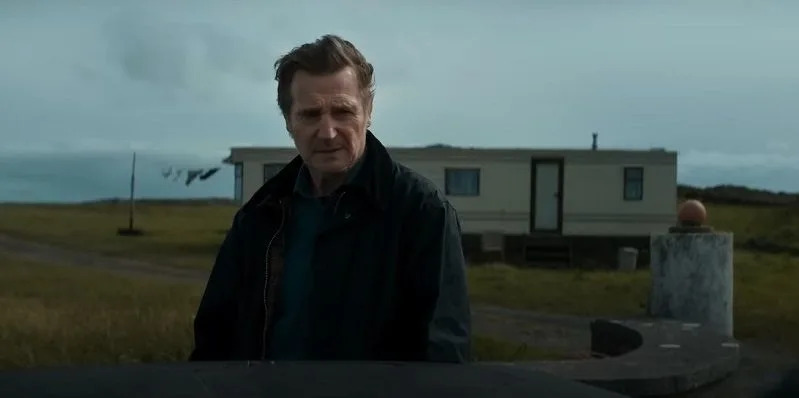 liam neeson in the land of saints and sinners movie, his character stands in front of a caravan and looks concerned