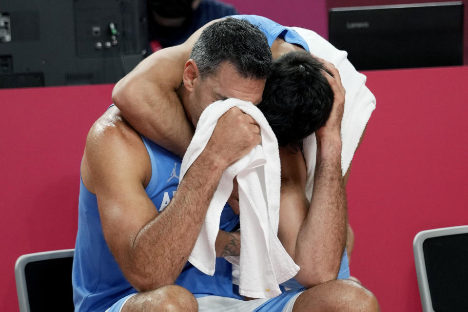 Argentina's Luis Scola (4) is hugged by teammate Facundo Campazzo as he receives an emotional standing ovation from his team, Australia players, and others in attendance when he was pulled from the game in the final moments of a men's basketball quarterfinal round game at the 2020 Summer Olympics, Tuesday, Aug. 3, 2021, in Saitama, Japan. (AP Photo/Eric Gay)