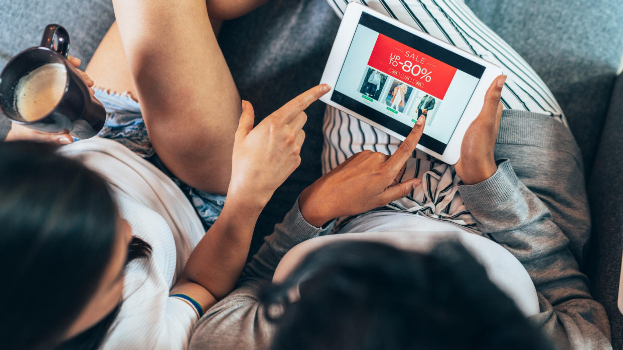 Two female friends drinking coffee and shopping online.