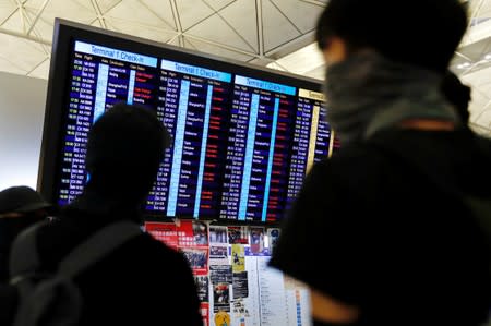 Anti-extradition bill protesters look at an information screen showing cancelled flights at Hong Kong International Airport as they attend a mass demonstration after a woman was shot in the eye during a protest in Hong Kong