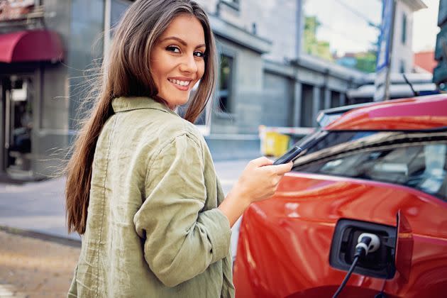 Portrait of woman starting charge process of her electric car using mobile phone (Photo: praetorianphoto via Getty Images)