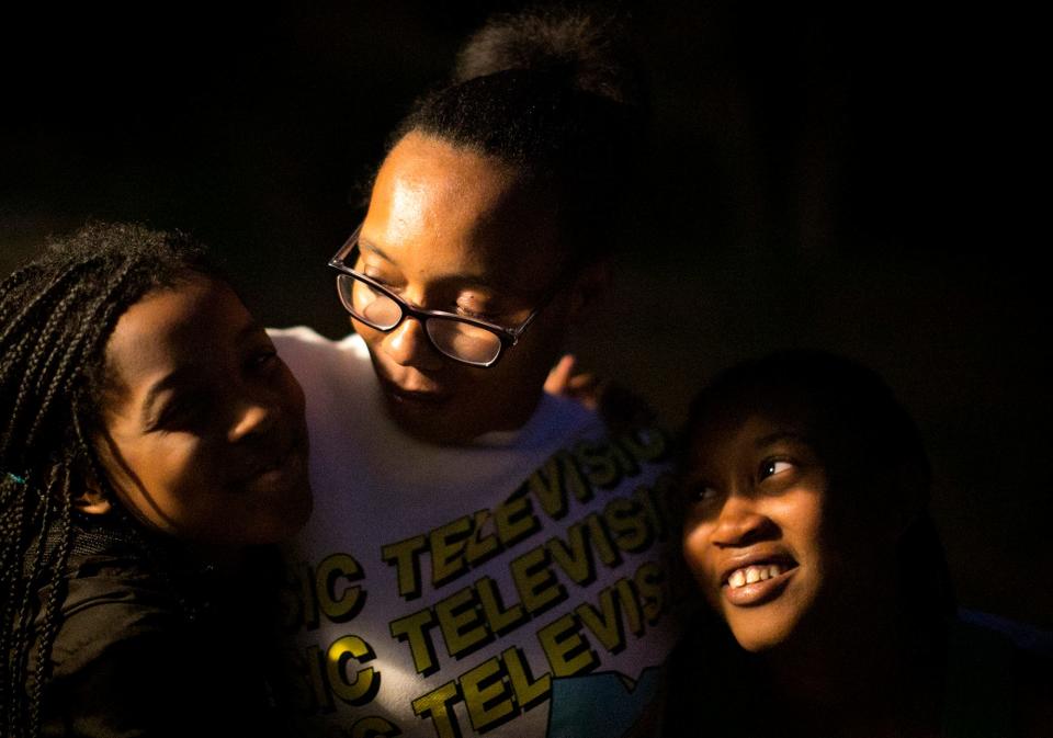 Armani Wells, 13, right and Arihanna Wells, 8, left, hug their mother, Cherise Harris, on their back porch in Painesville, Ohio, in October 2020. The family house is a block from a city-owned power plant, built in the 1800s, that still burns coal.