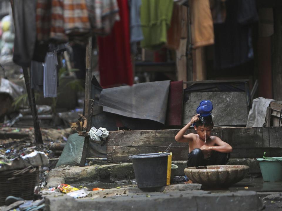 FILE - In this Thursday, Mar. 13, 2014, file photo, a boy takes a shower in a slum area in Jakarta, Indonesia. A report on inequality in Indonesia says its four richest men now have more wealth than 100 million of the country's poorest people. (AP Photo/Tatan Syuflana, File)