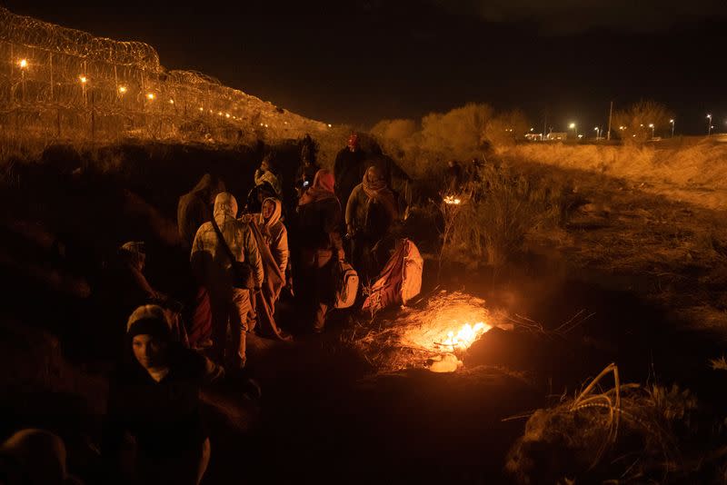 Migrants huddle near fire along the bank of the Rio Grande river in El Paso